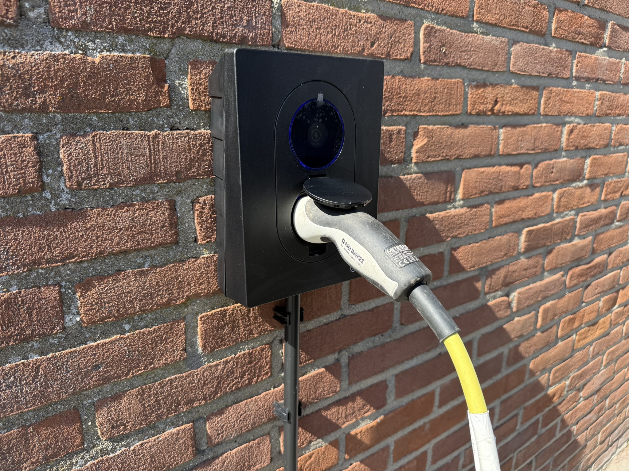 Zaptec laadpaal met laadkabel aangesloten op een bakstenen gevel in Hellevoetsluis